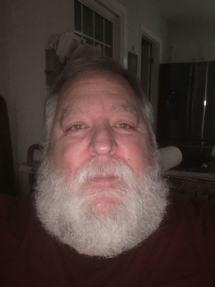 an older man with a long white beard wearing a red shirt and looking at the camera