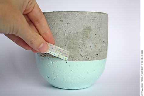 a hand is holding a small piece of paper in a cement cup with blue and white paint