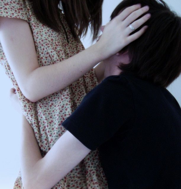 two people standing next to each other in front of a white wall and one person covering his face with her hands