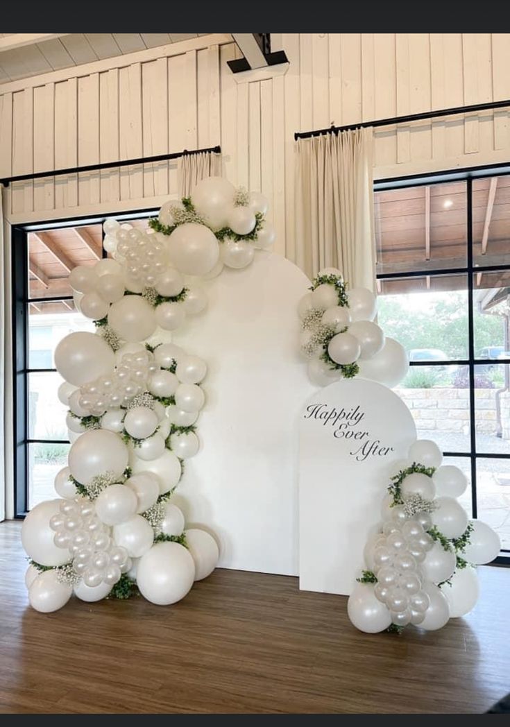 an arch made out of balloons and greenery is displayed in front of a window