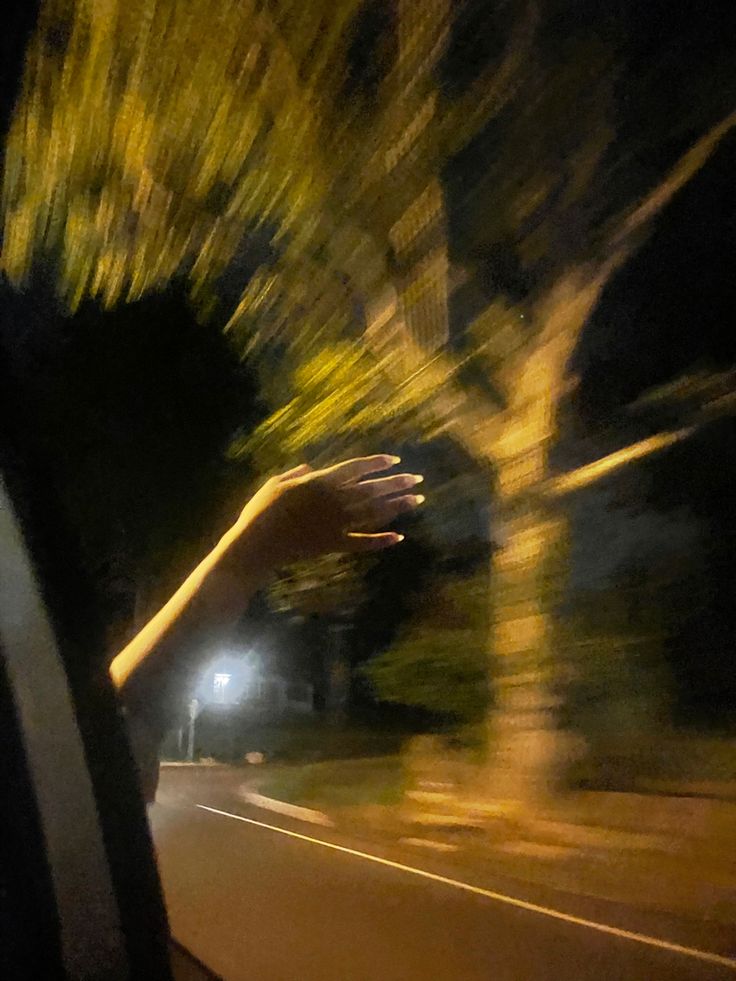 a person holding their hand out the window of a car at night with trees in the background