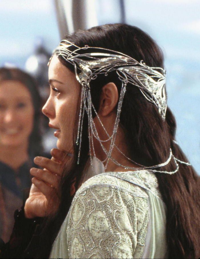 a woman with long hair wearing chains around her head and looking off into the distance