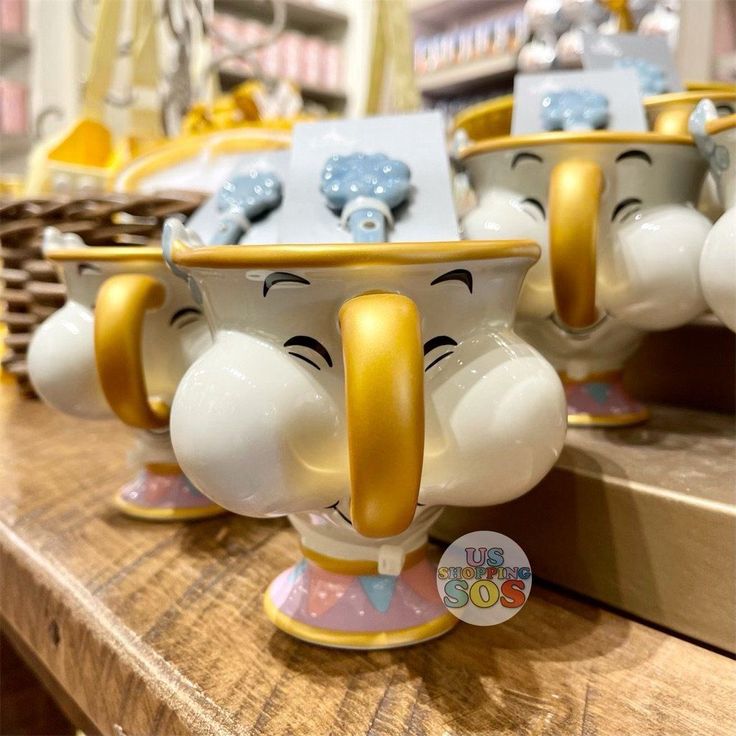 two ceramic cups with faces on them sitting on a table in front of other mugs