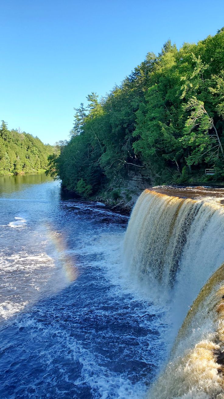 a large waterfall with a rainbow in the middle of it's water fall, surrounded by lush green trees