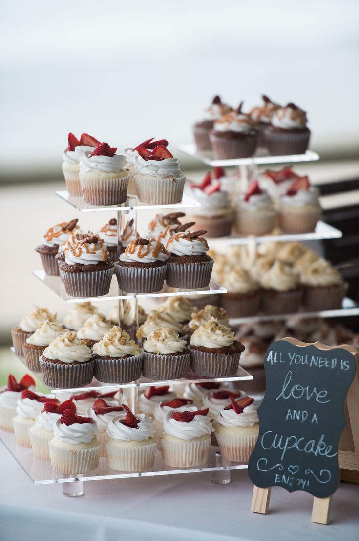 cupcakes are arranged on three tiered trays with a chalkboard sign next to them