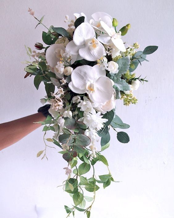 a bouquet of white flowers and greenery being held up by someone's hand