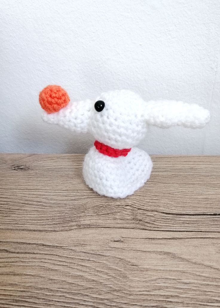 a crocheted white dog with an orange ball in its mouth sitting on a wooden surface