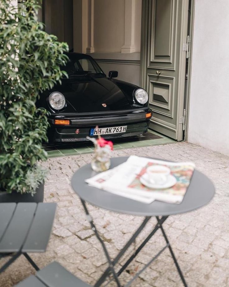 a small table with a magazine on it next to a black porsche parked in front of a building