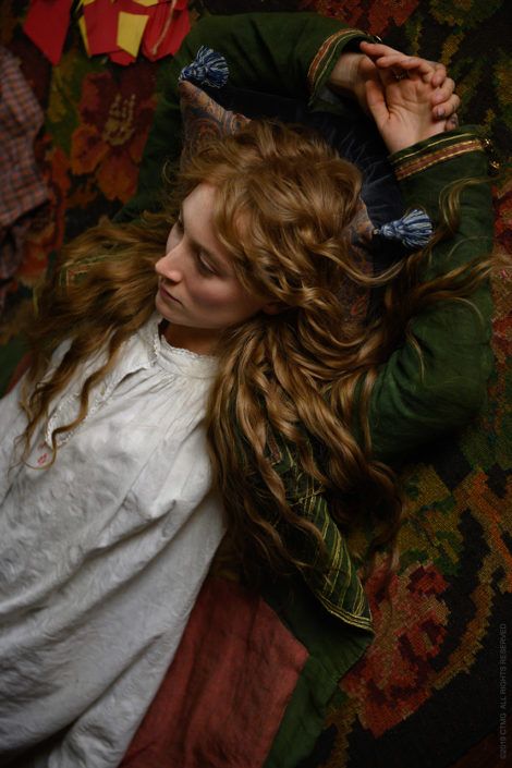 a woman laying on top of a couch next to a red and green blanket with her hair blowing in the wind