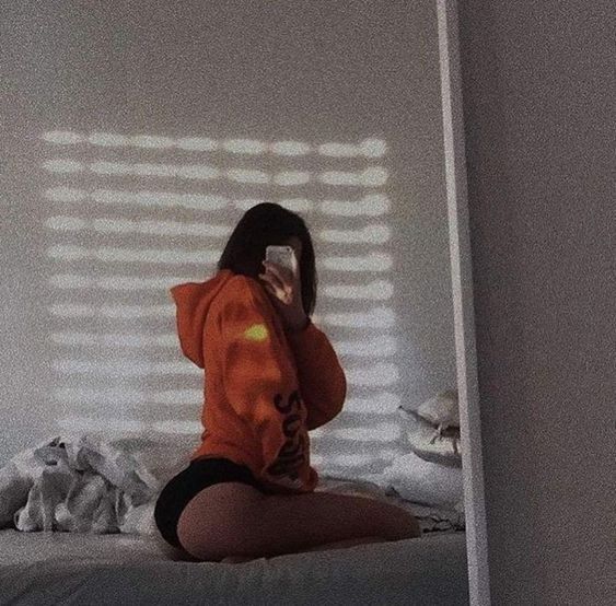 a woman sitting on top of a bed taking a selfie