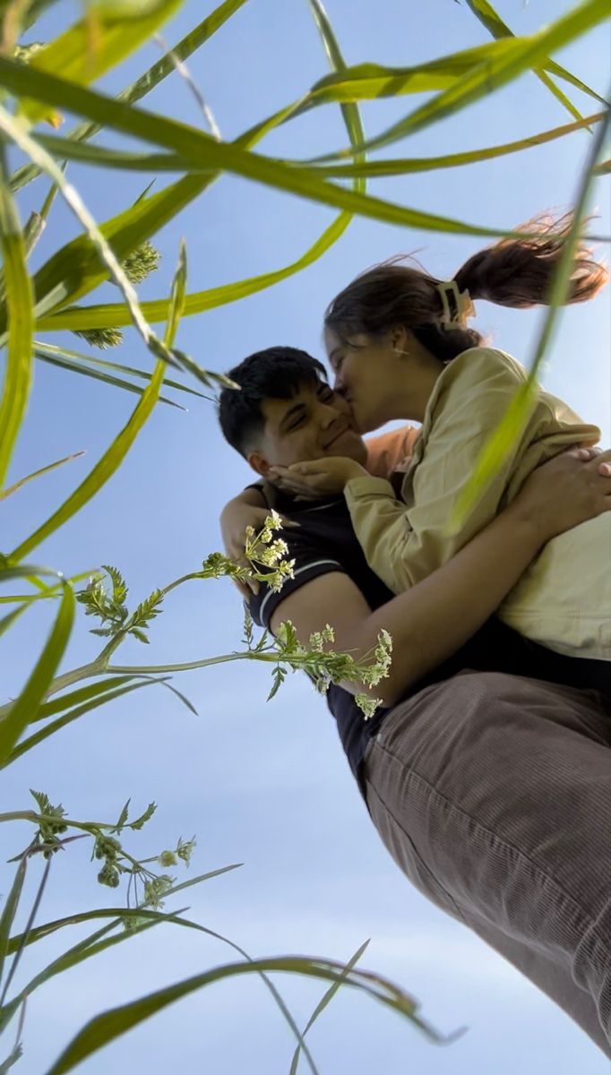 a man and woman embracing each other in front of blue sky with green leaves on the branches