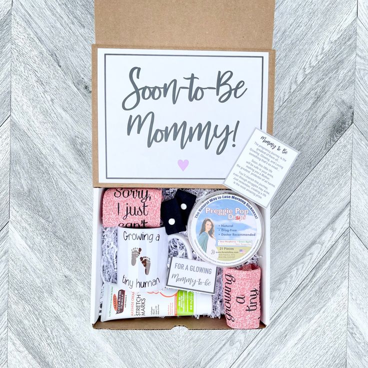 a box filled with lots of different items on top of a wooden floor next to a sign that says, soon to be mommy