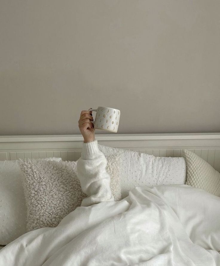 a person laying in bed holding a cup above their head