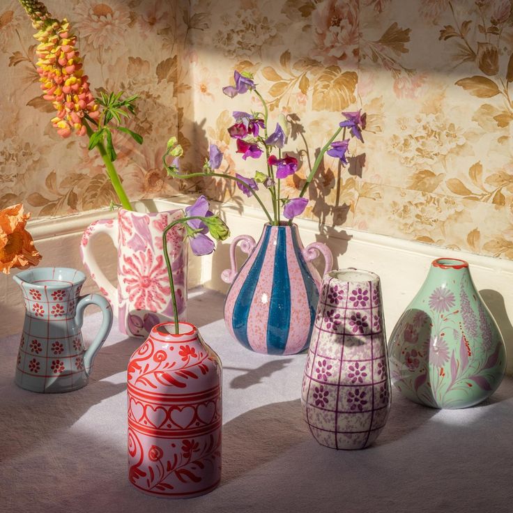 several vases with flowers in them sitting on the floor next to a wallpapered wall