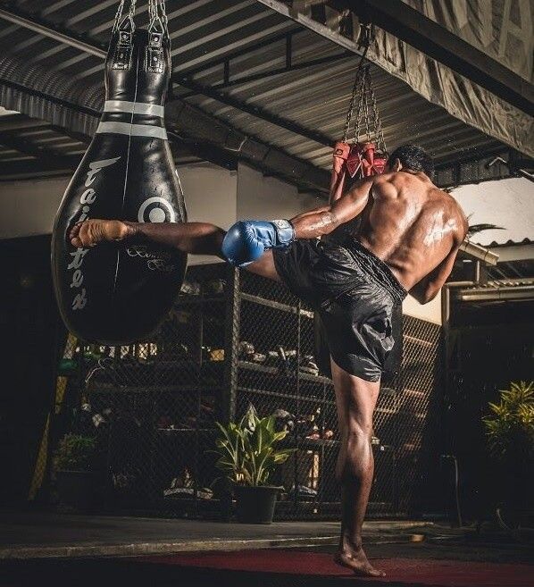 a man in black shorts and boxing gloves kicking a punching bag