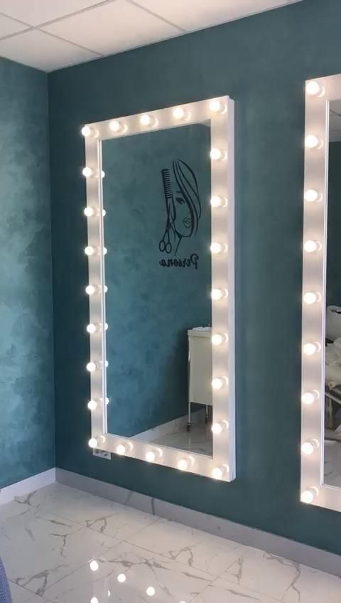 a bathroom mirror with lights on it in front of a blue wall and white tile floor