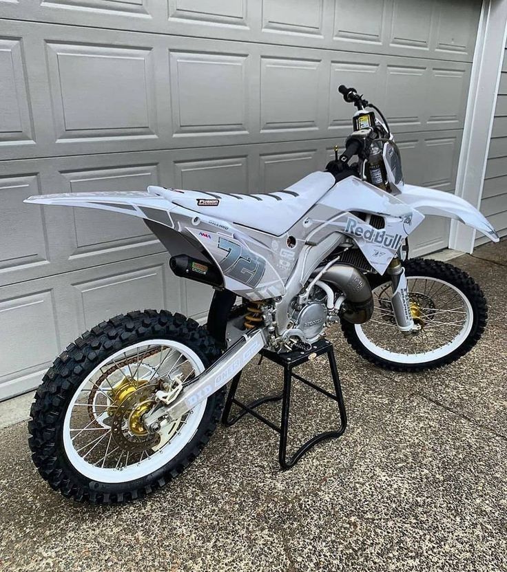 a white dirt bike parked in front of a garage