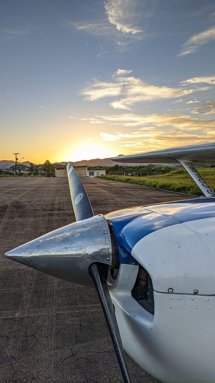 an airplane sitting on the tarmac with the sun setting in the distance behind it