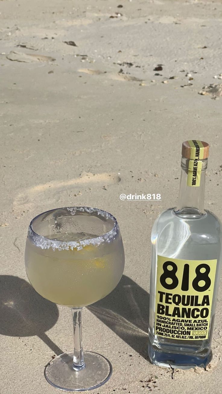 a bottle of tequila next to a glass on the beach