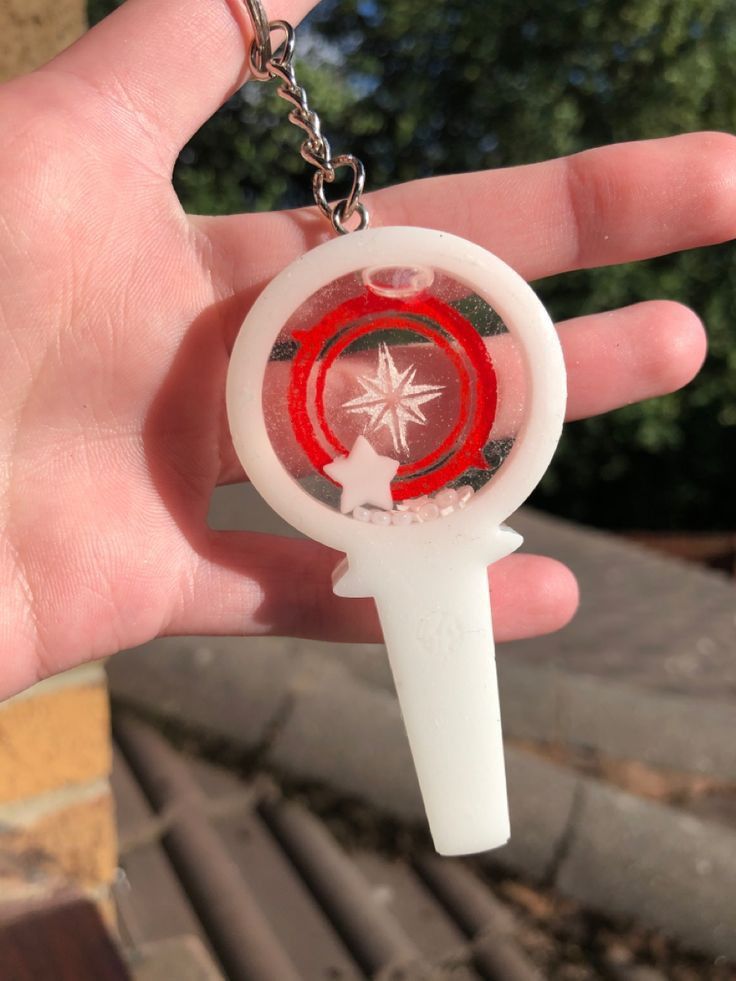 a hand holding a keychain with a red and white design on it