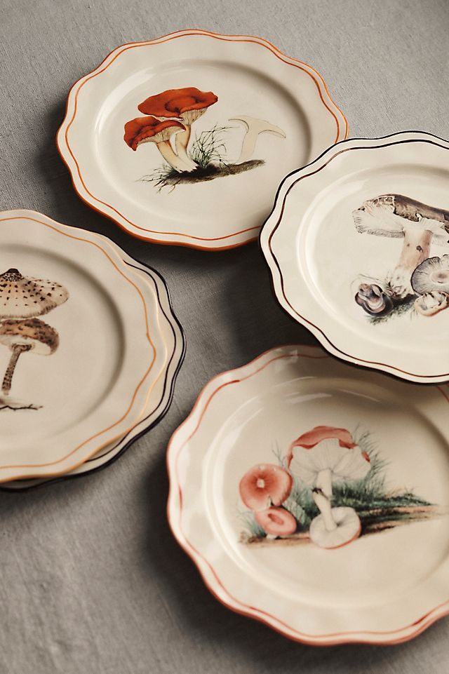 four plates with different designs on them sitting on a tableclothed surface, one has mushrooms and the other has an orange mushroom