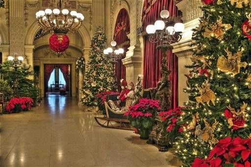 christmas trees are lined up in the lobby of a building with chandeliers hanging from the ceiling