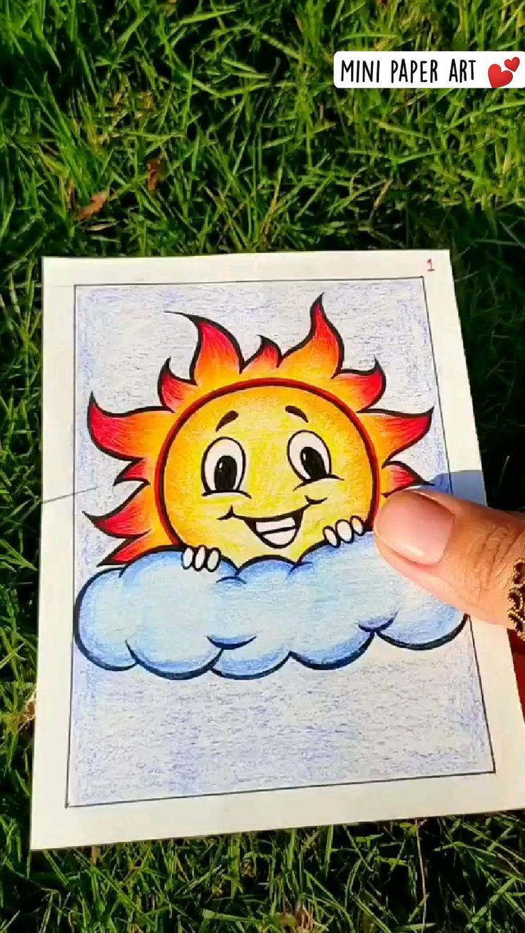 someone's hand holding up a drawing of a sun on top of a cloud