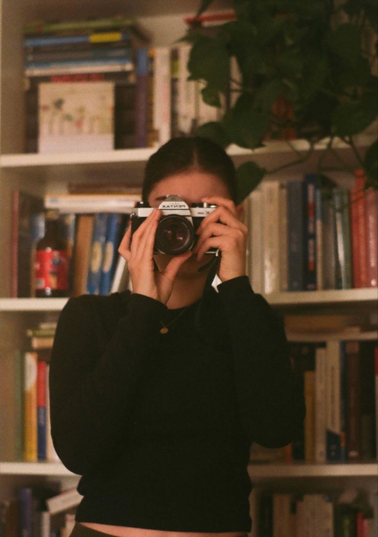 a woman taking a photo in front of a bookshelf with her old camera