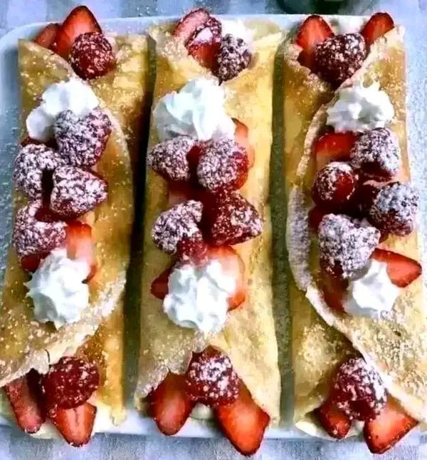 three crepes with strawberries and powdered sugar on them