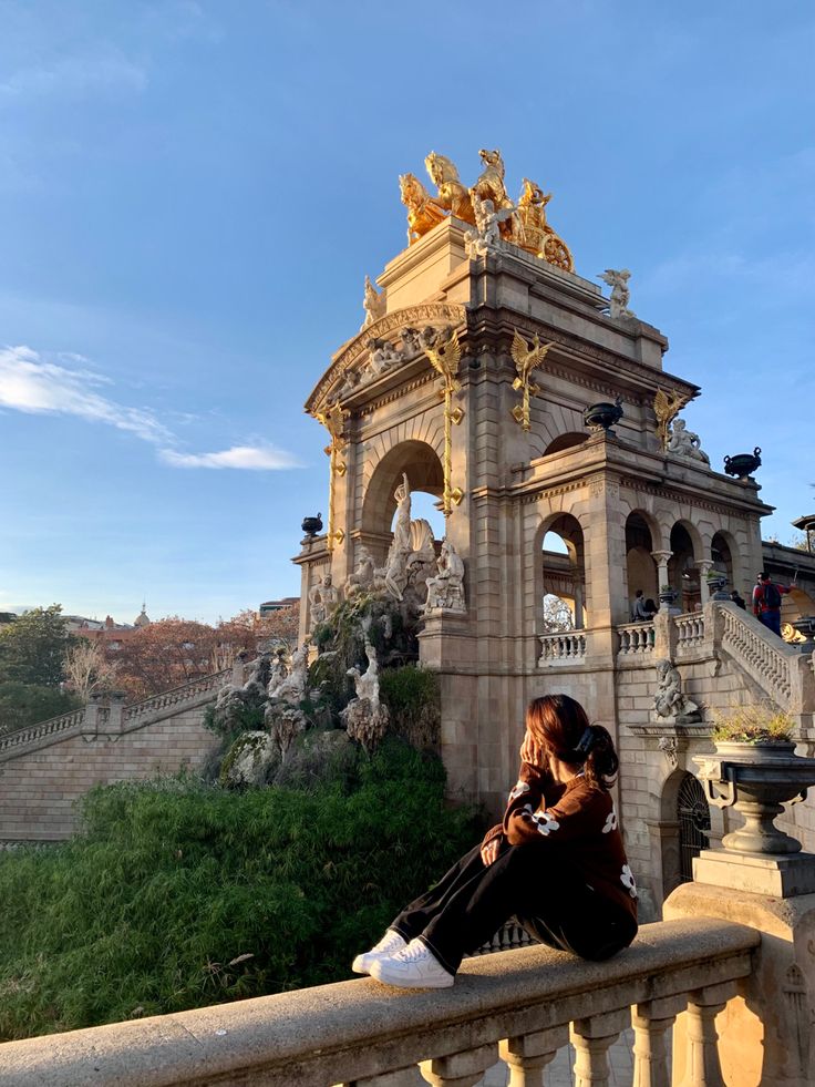 a woman sitting on top of a stone wall next to a tall building with statues