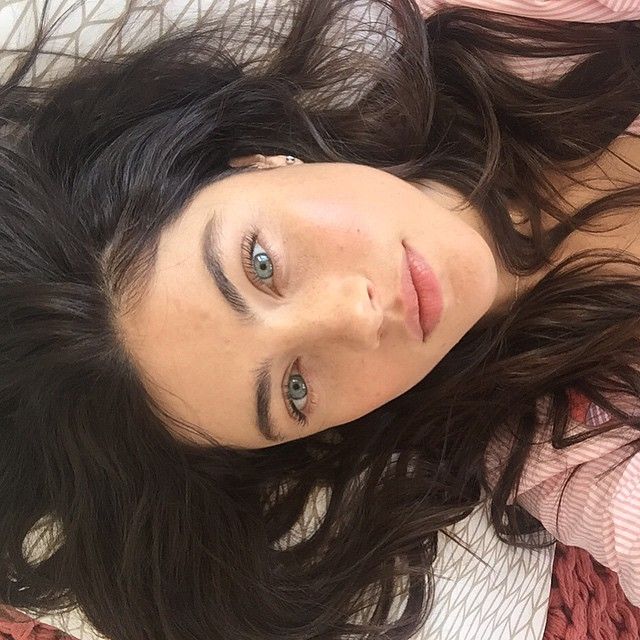 a woman laying on top of a bed next to a red and white blanket with her hair blowing in the wind