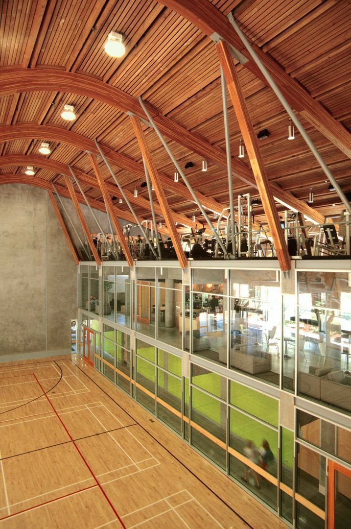 an indoor basketball court with wooden ceiling and glass windows on both sides, surrounded by wood flooring