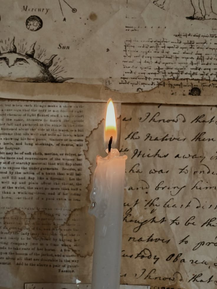 a lit candle sitting on top of a table next to an old piece of paper