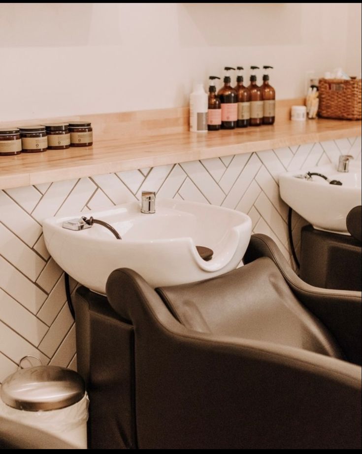 two white sinks sitting next to each other in a room with bottles on the wall