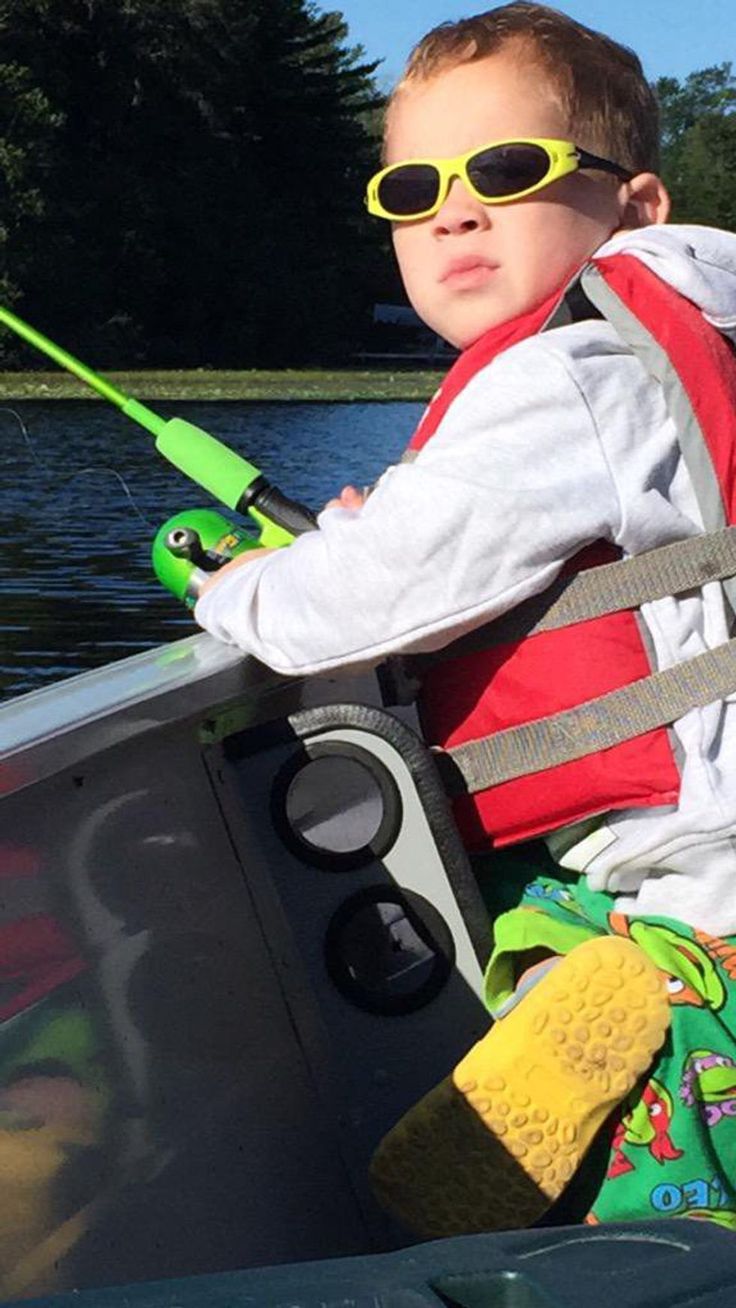 a young boy in sunglasses and life jacket sitting on the back of a boat holding a fishing pole