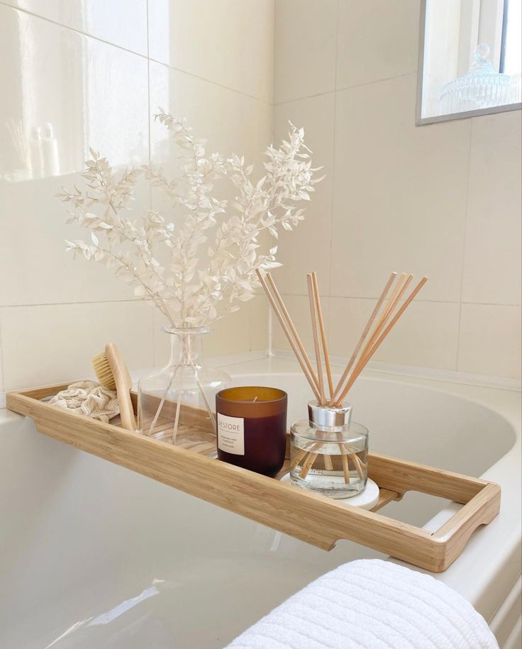 a wooden tray with candles and reeds in it on a bathtub next to a white towel