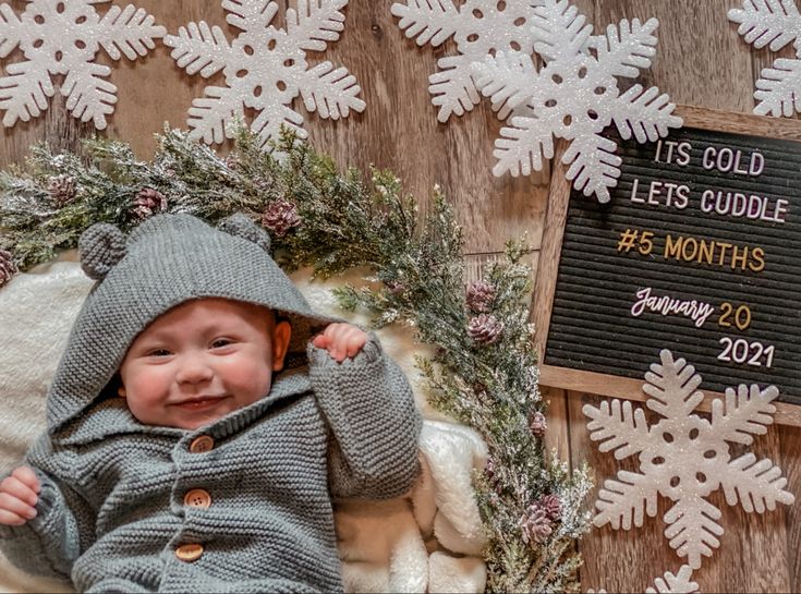 a baby is laying in front of snowflakes and a sign that says it's cold let's cuddle