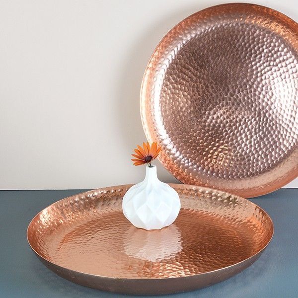 an empty vase sitting on top of a shiny metal tray next to a large copper platter