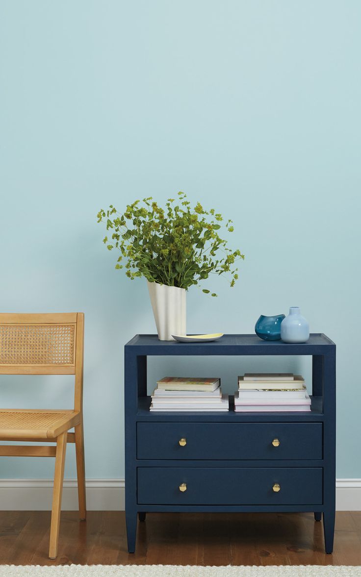 a blue table with two drawers and a plant on it next to a wooden chair