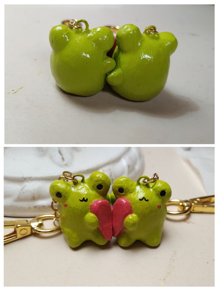 two green frog keychains with red heart on each one and gold chain attached to them