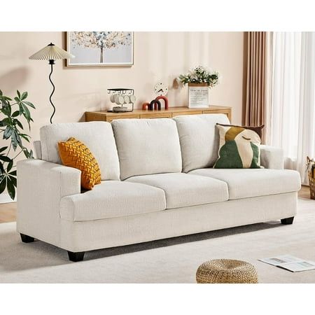 a living room scene with focus on the sofa and pillows in the foreground, along with potted plants