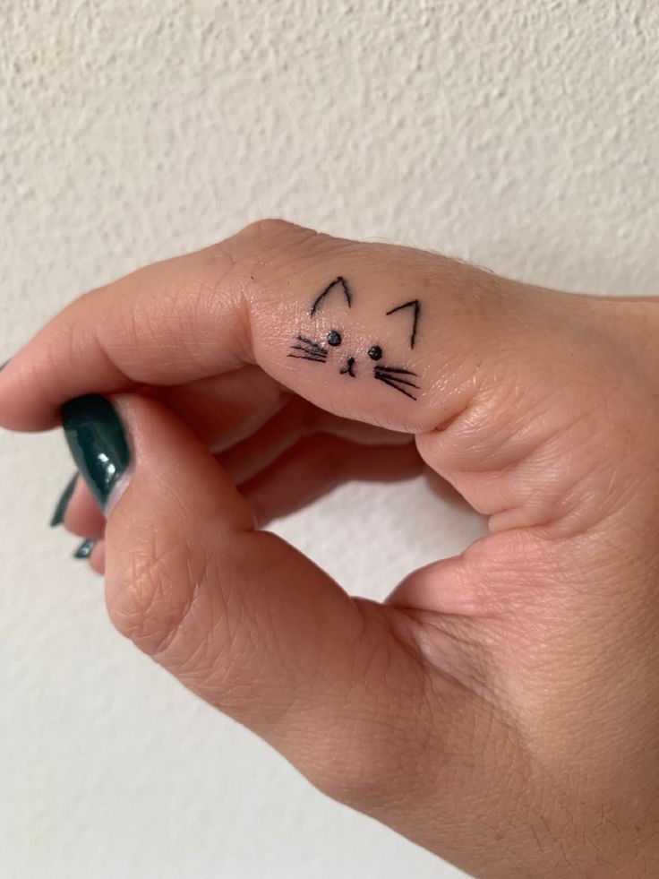 a person's hand with a small cat tattoo on their left thumb and finger