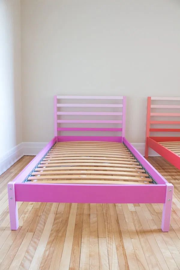 two beds with pink frames and wooden slats in a room, one is empty