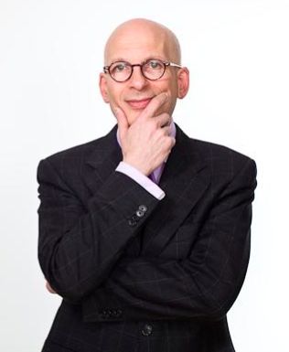 a man in a suit and glasses is posing for the camera with his hand on his chin