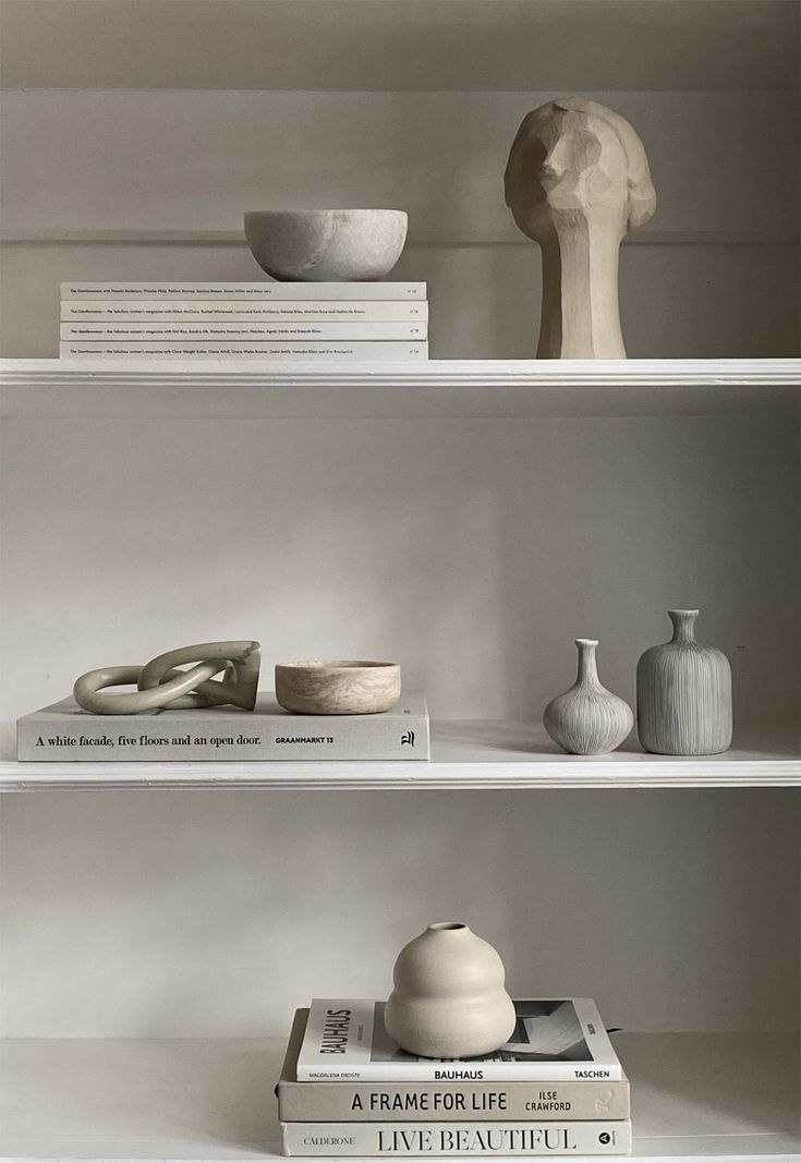 three white shelves with vases and books on them