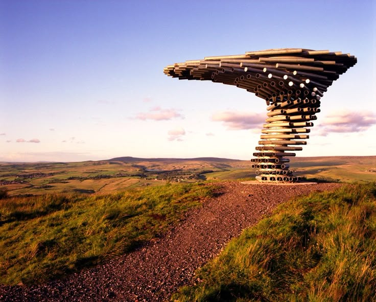 a wooden structure on top of a hill in the middle of a grassy field with hills behind it