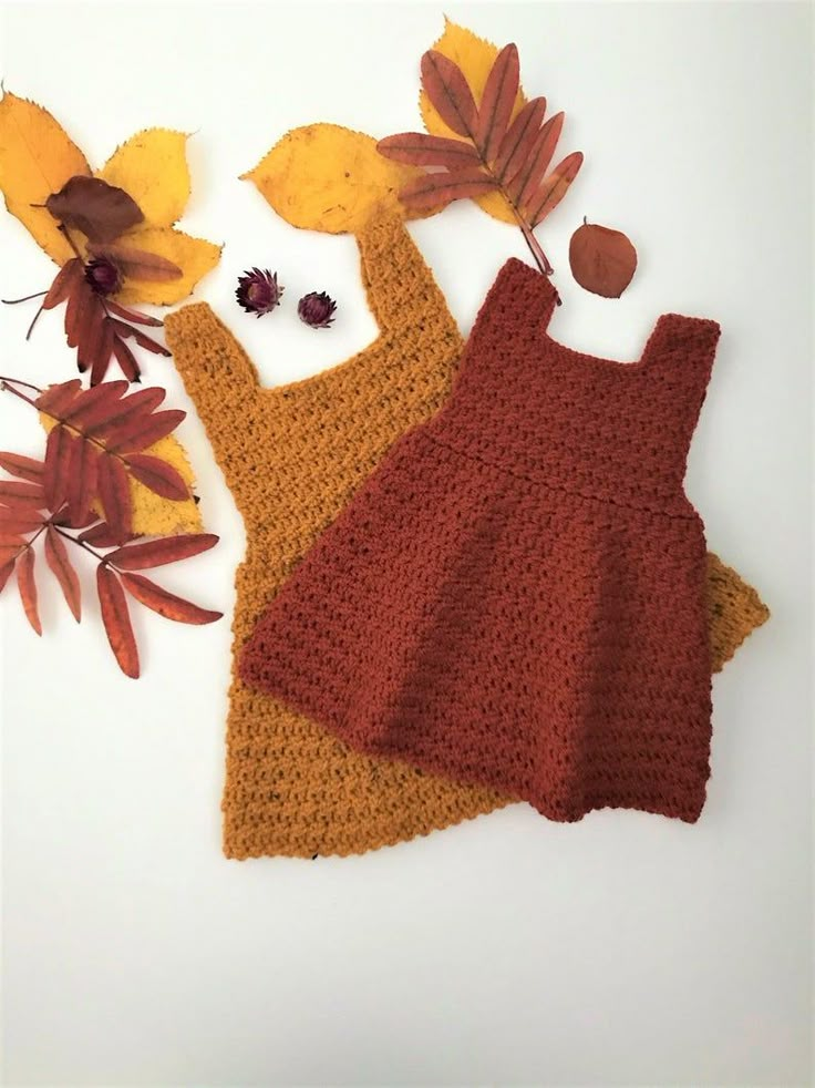 two crocheted aprons sitting on top of each other next to autumn leaves