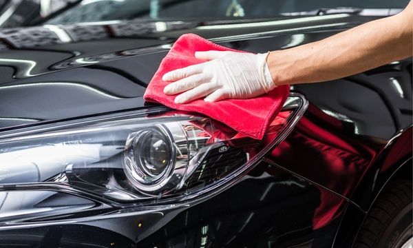 a person wiping the hood of a black car with a red microfibrel