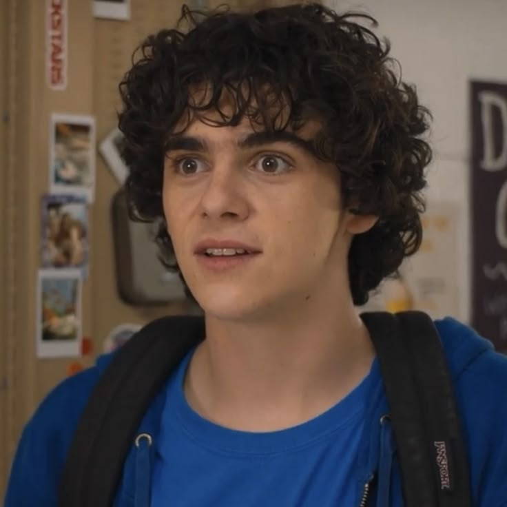 a young man with curly hair wearing a backpack