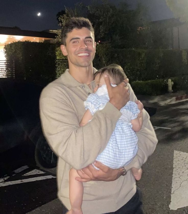 a man is holding a baby in his arms and smiling at the camera while standing outside